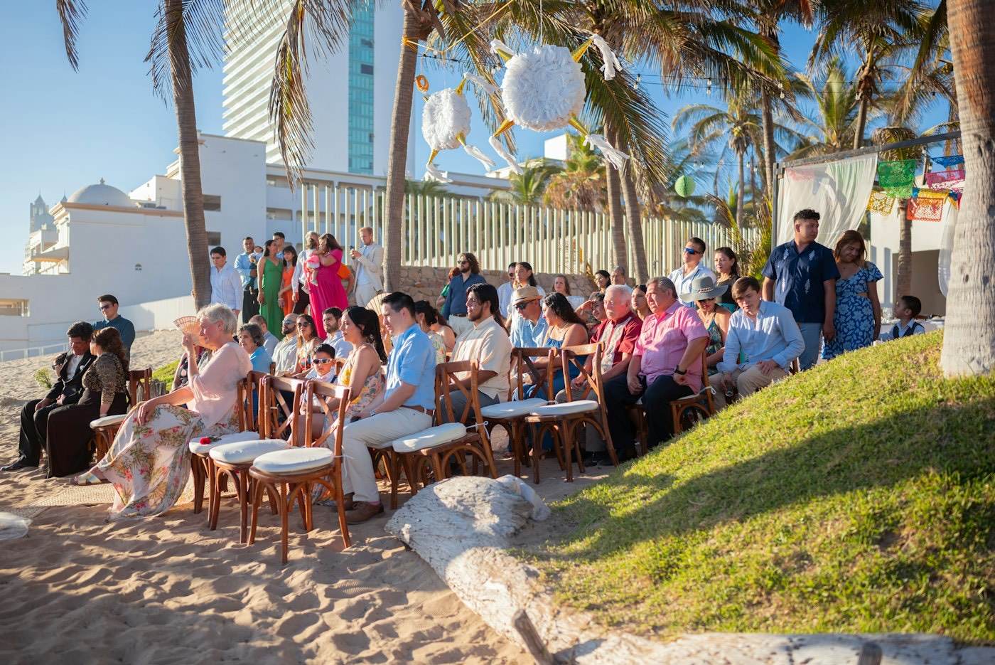Des invités assis sur de simples chaises en bois posées sur le sable pour une cérémonie de mariage à la plage au soleil