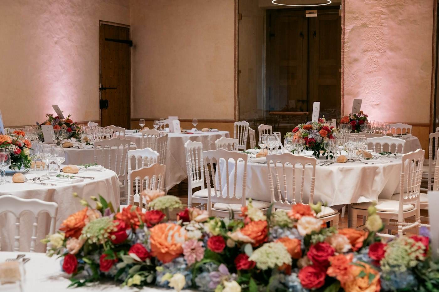 Round wedding reception tables with full florist arrangements of roses and hydrangeas in orange, red and blue