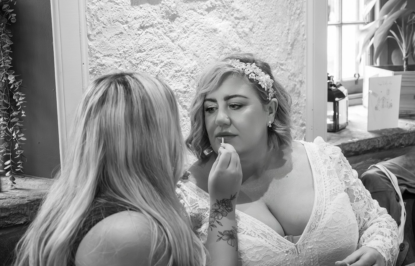 Eine Visagistin trägt einer Braut im Spitzenkleid mit Perlen-Haarschmuck Lippenfarbe auf