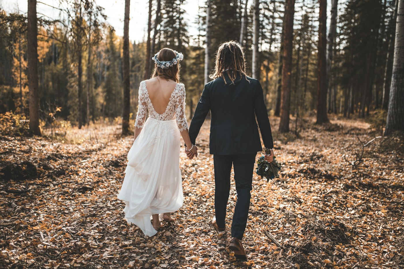 Brautpaar geht Hand in Hand durch einen Herbstwald voller Laub