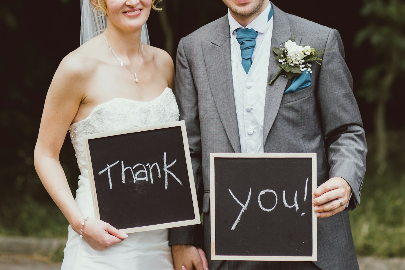 Braut und Bräutigam stehen nebeneinander und halten zwei kleine Kreidetafeln mit der Aufschrift Thank you
