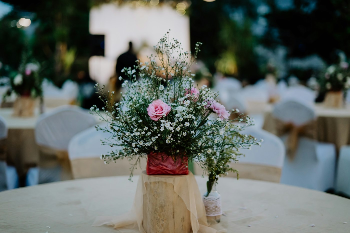 Un centre de table simple de gypsophile et de roses roses sur une rondelle de bois, chaises nouées d’un ruban