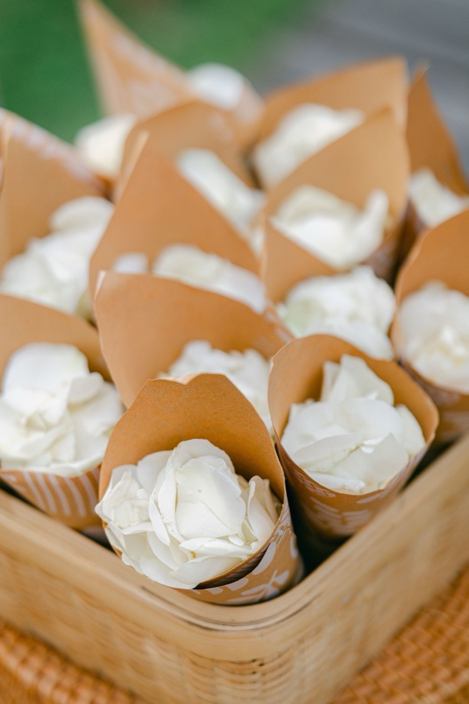 Kraft paper cones filled with white rose petals, standing upright in a wooden tray, ready for the wedding exit